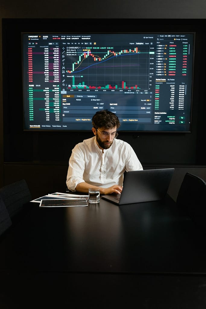 Man on computer with data viz on large screen